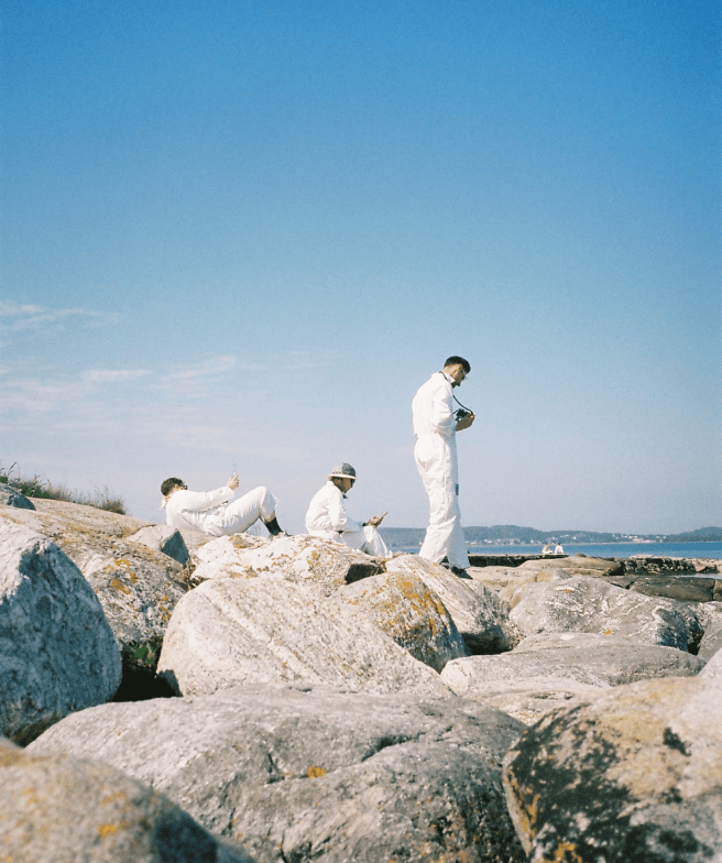 Analog photo of three people in white coats on rocks next to a sea