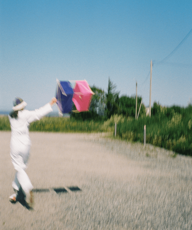 A slightly blurry image of a person in a white coat running with their custom-made kite in the air behind them