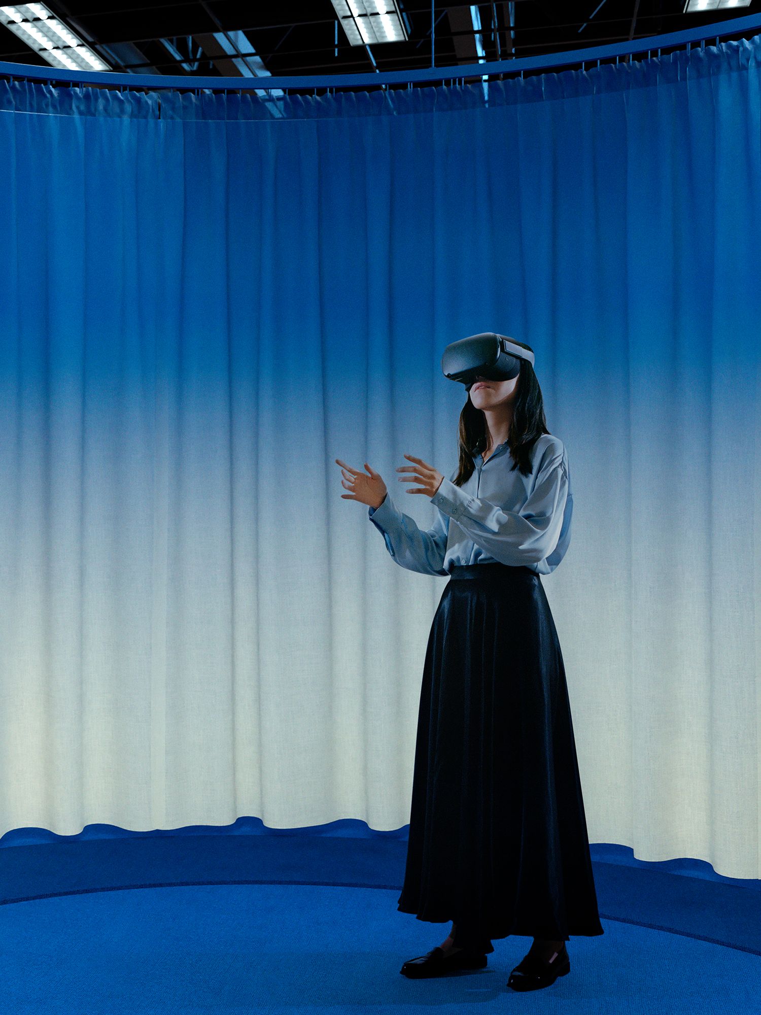 Image of a woman using a VR headset in a room with a blue floor and curtains with a blue to white gradient