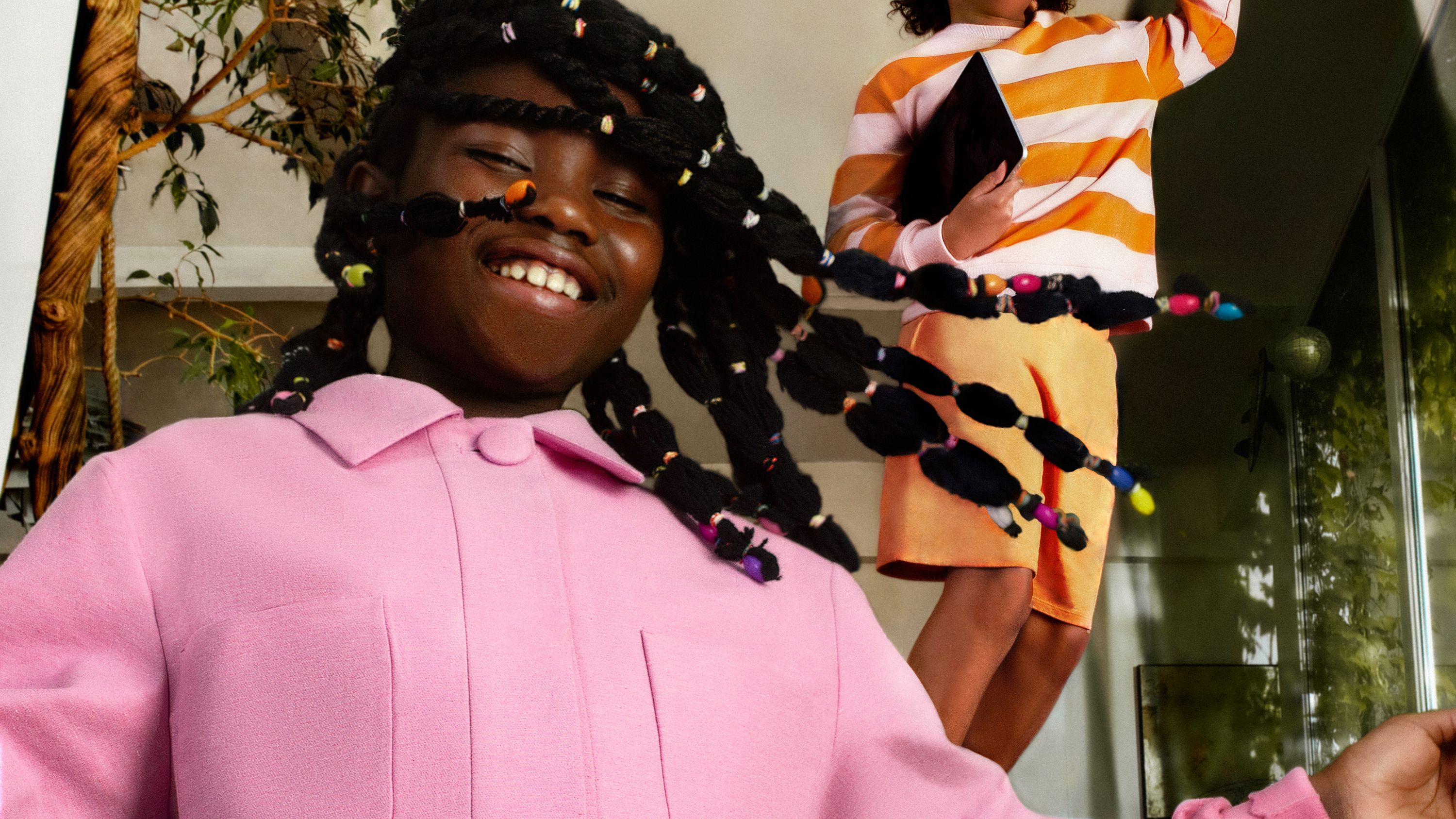 Portrait of a smiling child dancing in a pink coat. In the background another child dances while holding an iPad.