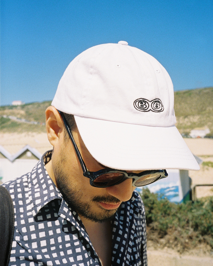 A man wearing a white cap, checked shirt. Natural landscape at the back.
