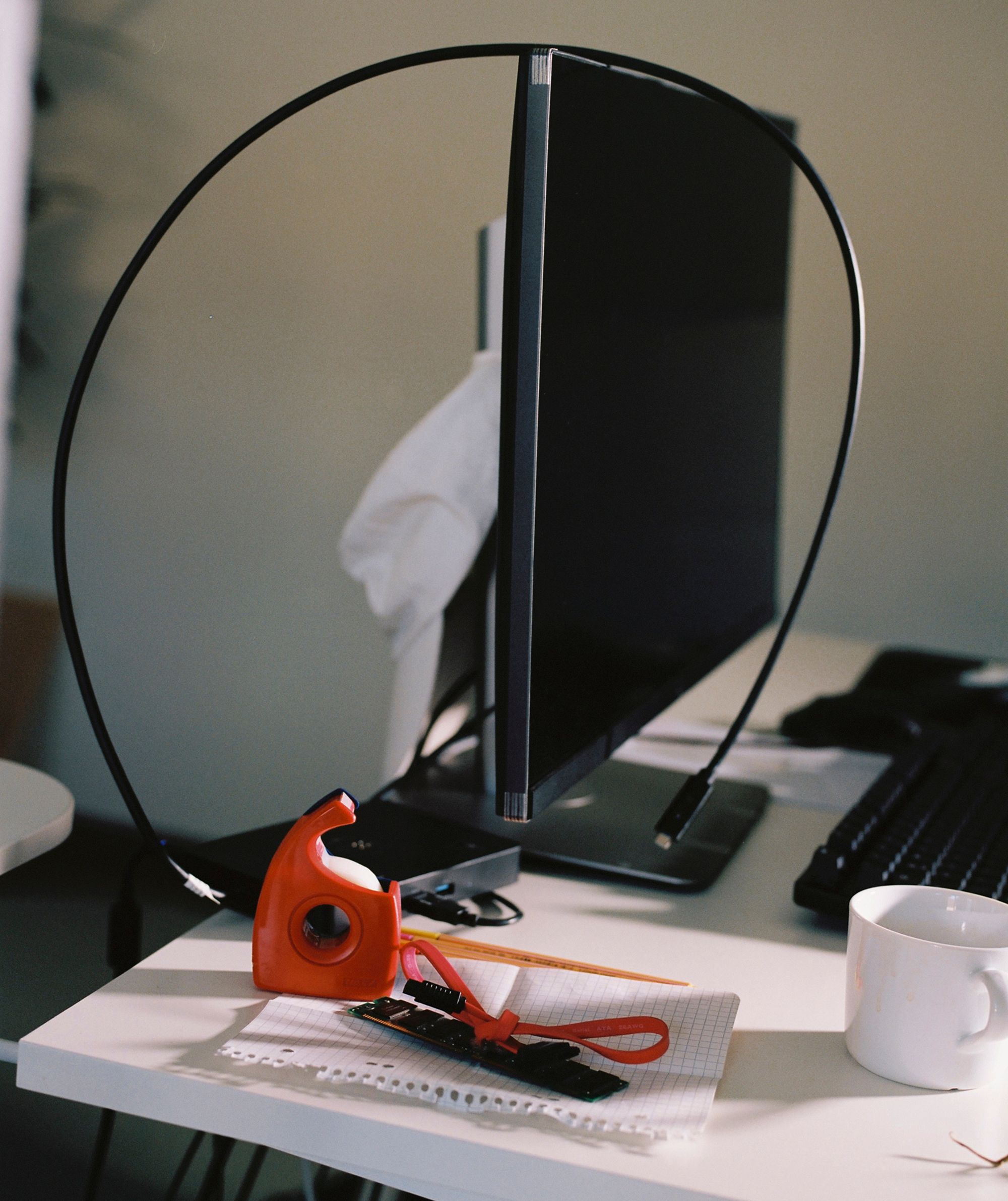 A messy desk, including a coffee cup and a computer screen with a cable hanging over it