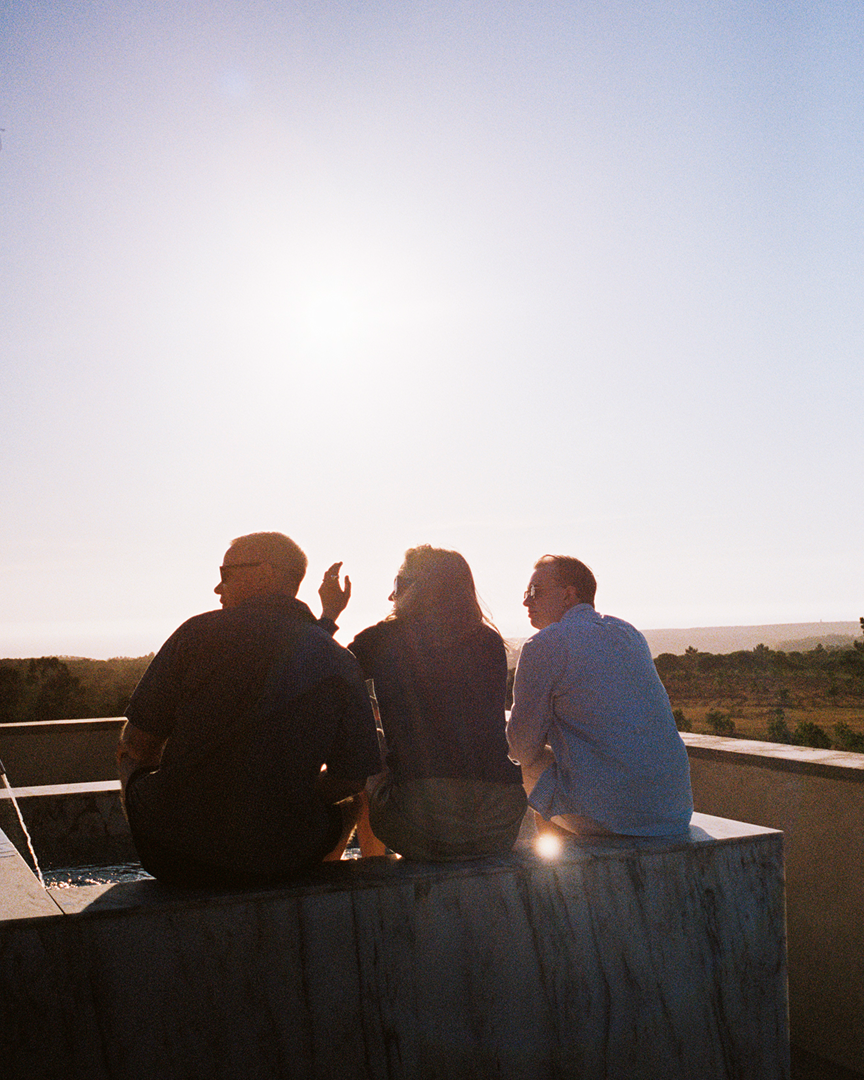 Three people sitting on a concrete surface, facing backwards.