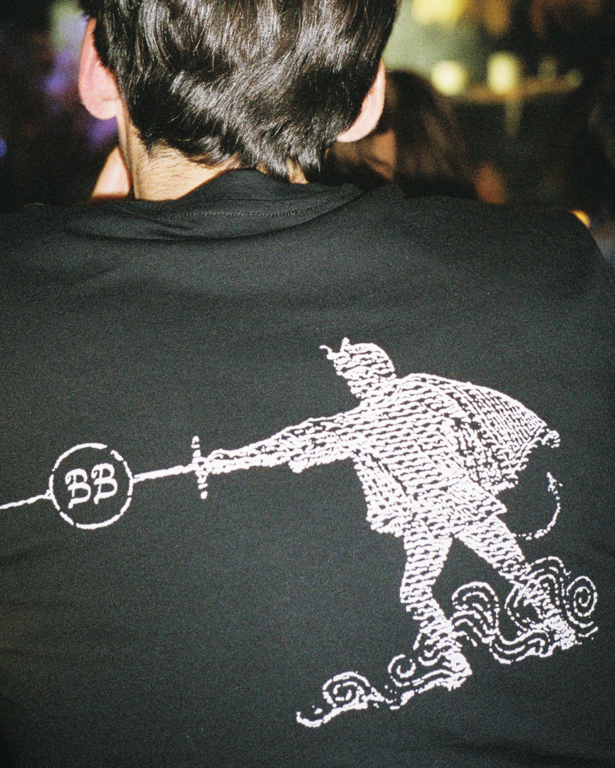 A man seen from the back, he wears a branded black tshirt.