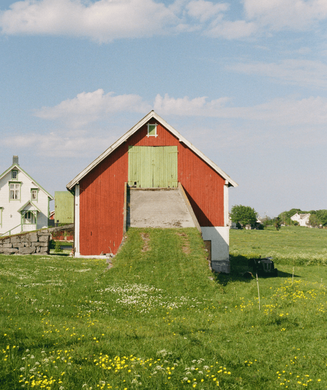 A wooden house with a gabled roof surrounded by grass. The house seems to be used as a storage location and is painted in bright red