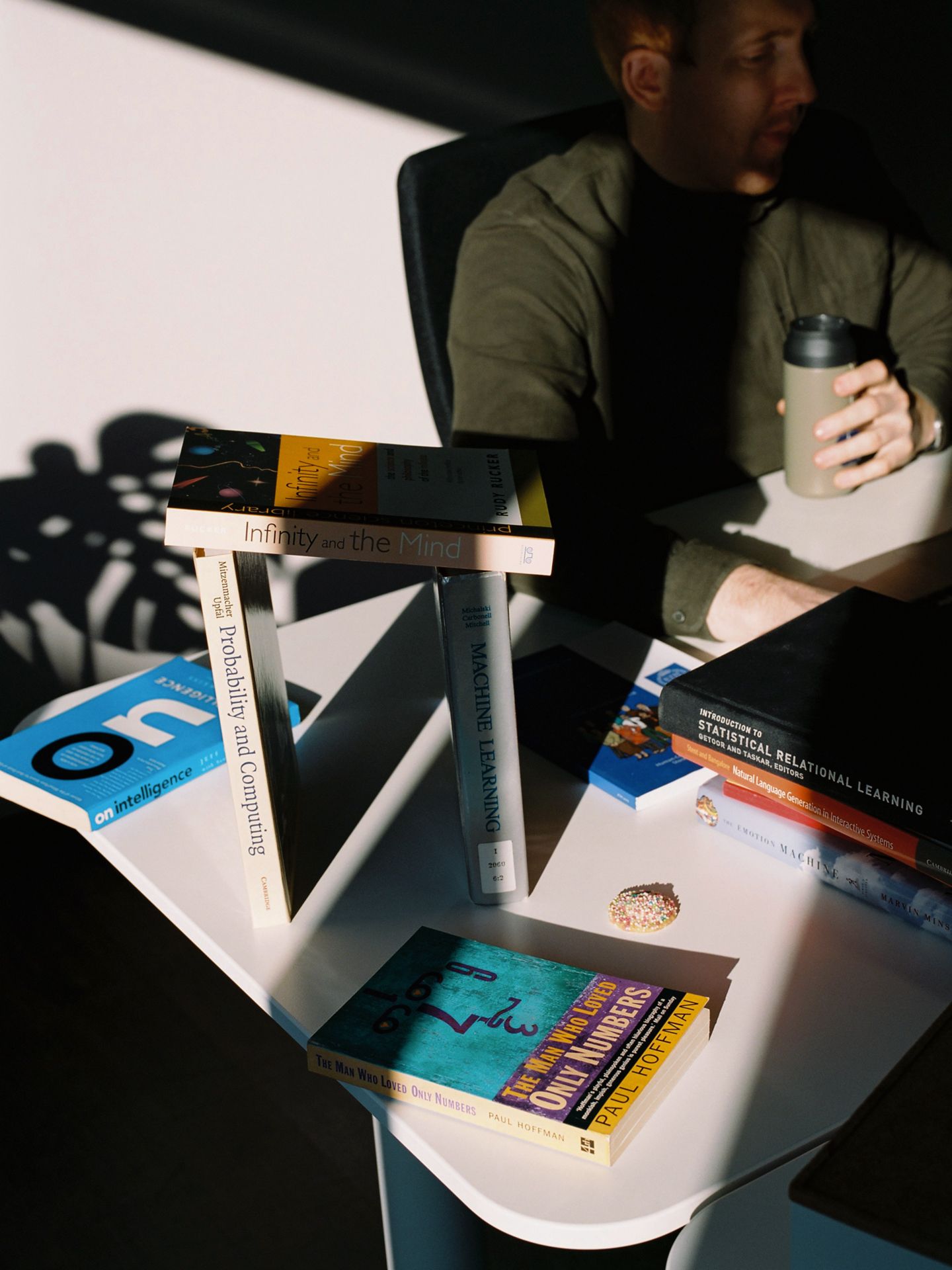 A desk full of books that cast shadows due to the sun coming in from the side