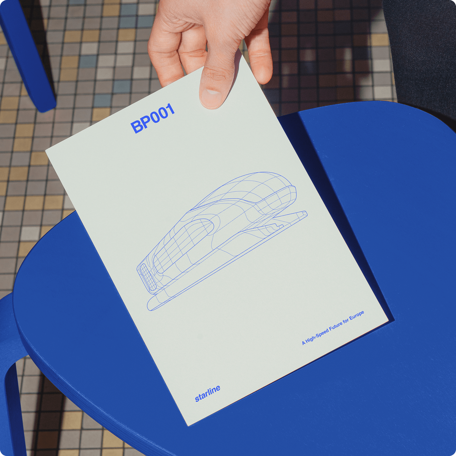 Mock up of a hand holding the train's blueprint, with BP001 as a title, on a blue stool
