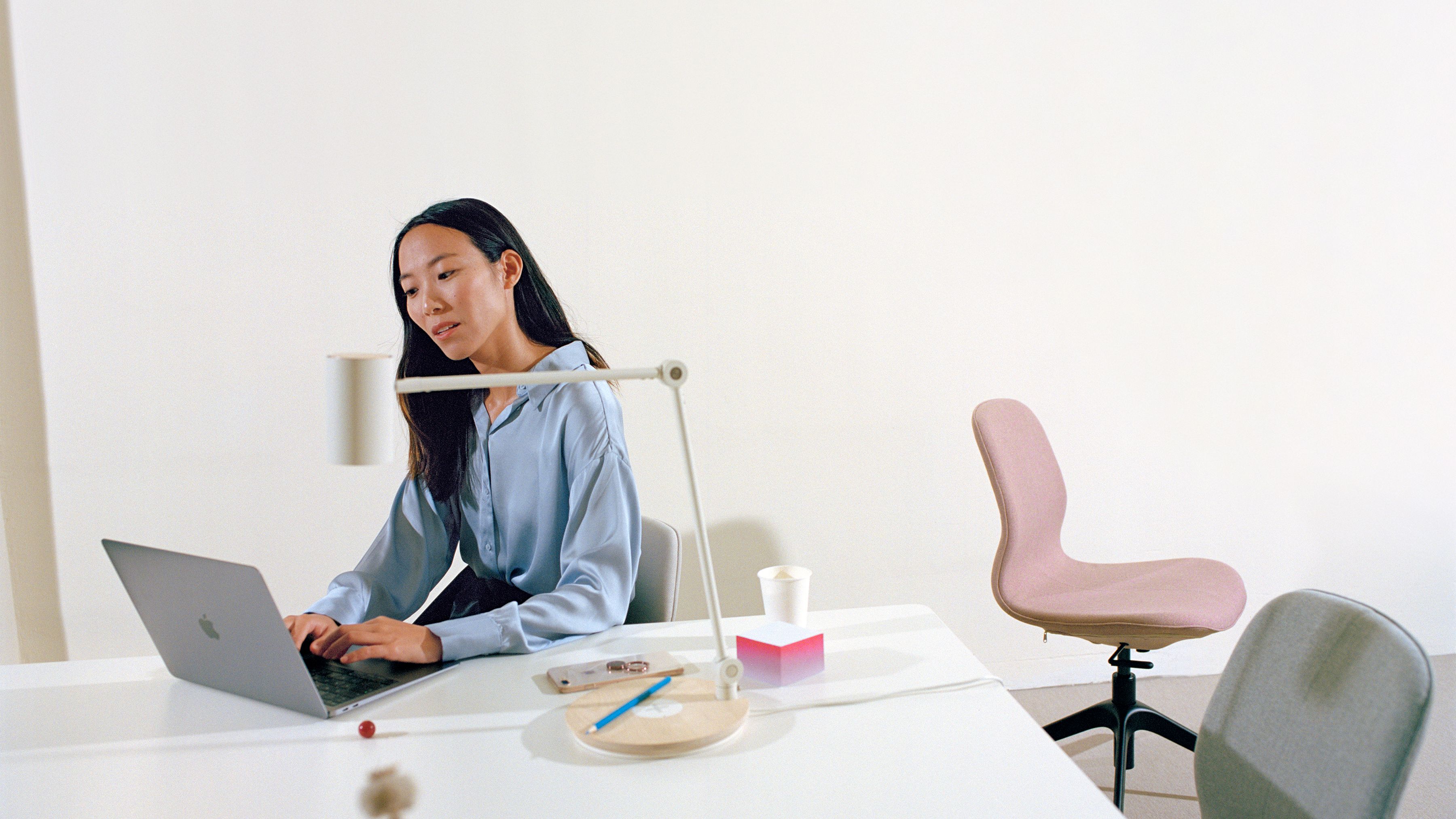 Woman sitting at desk behind a laptop, with two empty office chairs on her left side.