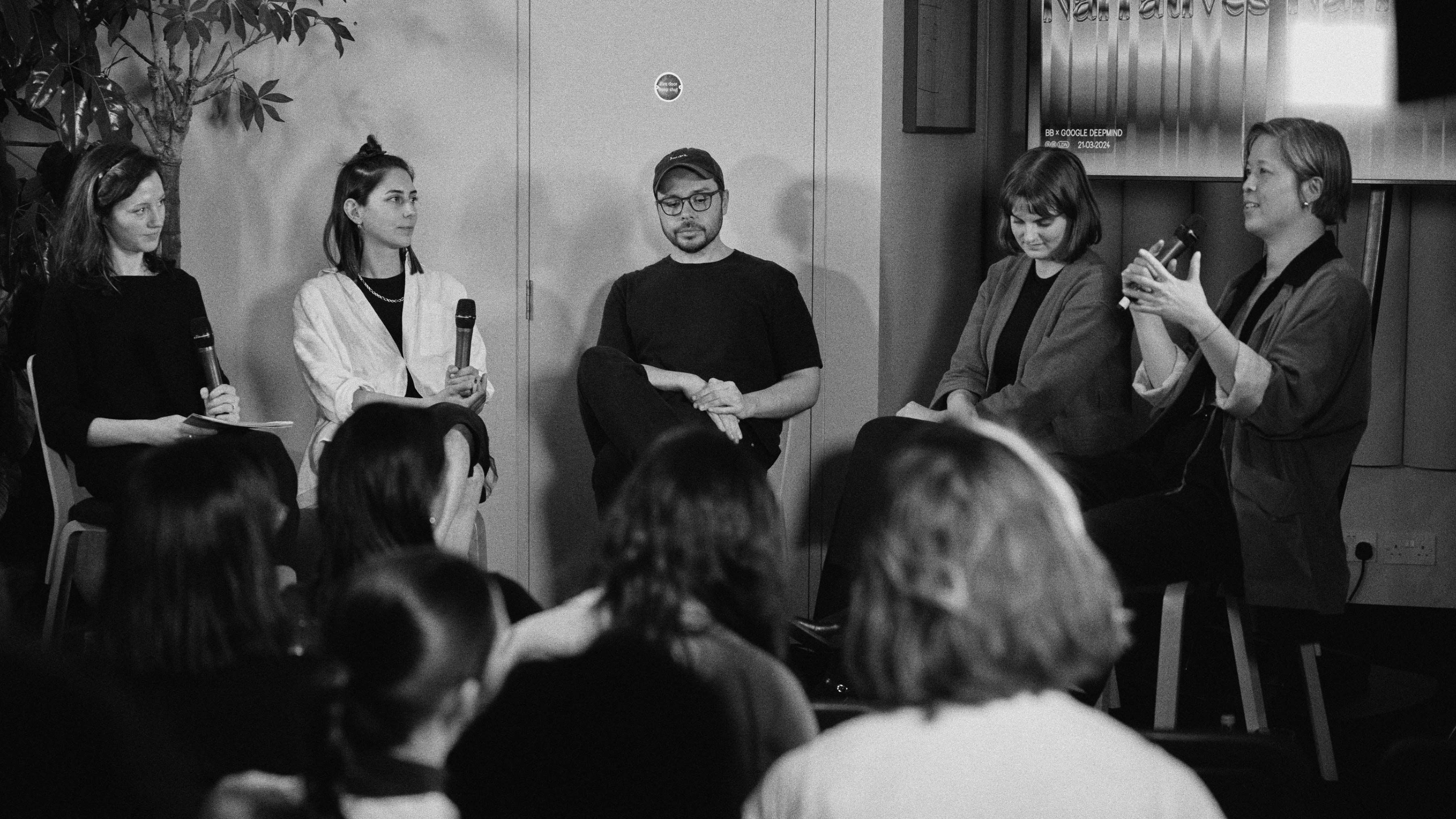 Photo of the four speakers and moderator, seated on chairs. Amelie Dinh speaks in her microphone.